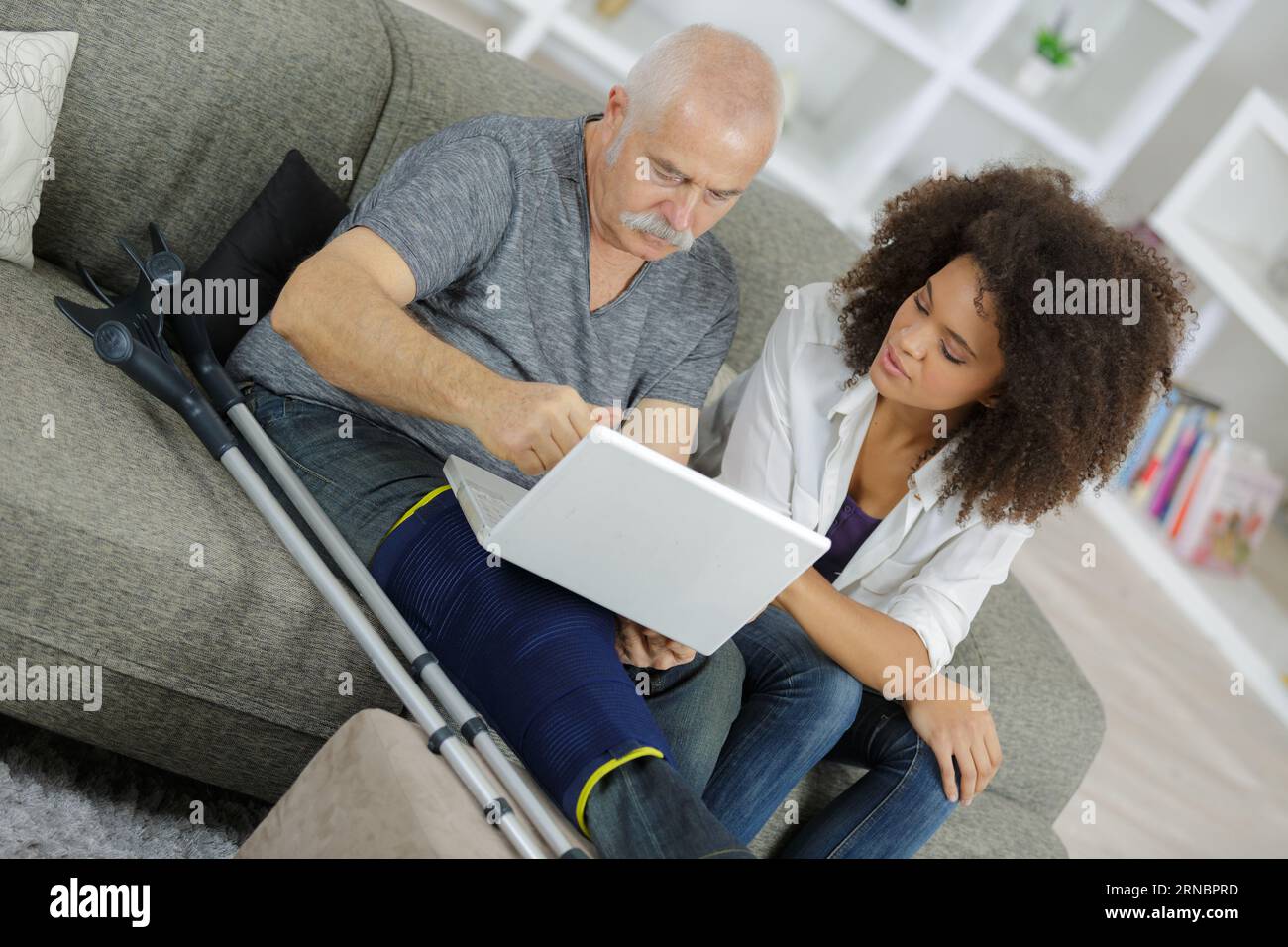 senior man with injured leg showing pc to carer Stock Photo - Alamy