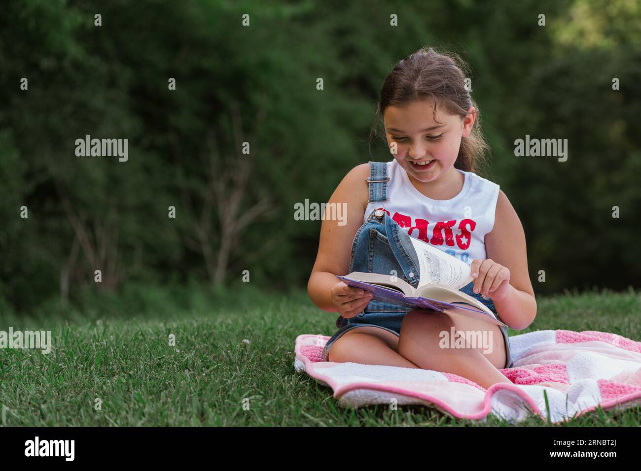 A young girl sitting on a blanket reading a book Stock Photo