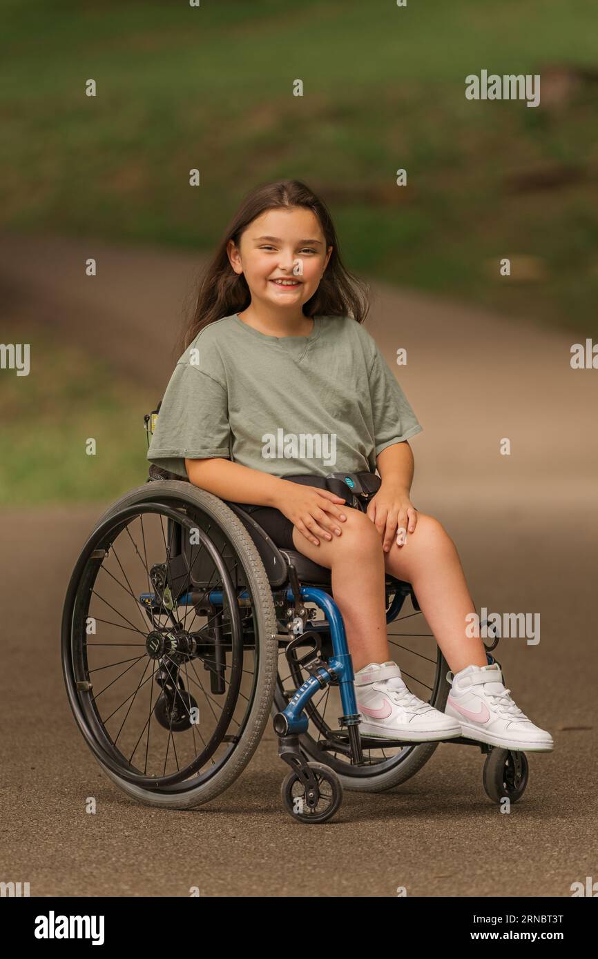 A young lady smiling in a wheelchair at a park Stock Photo
