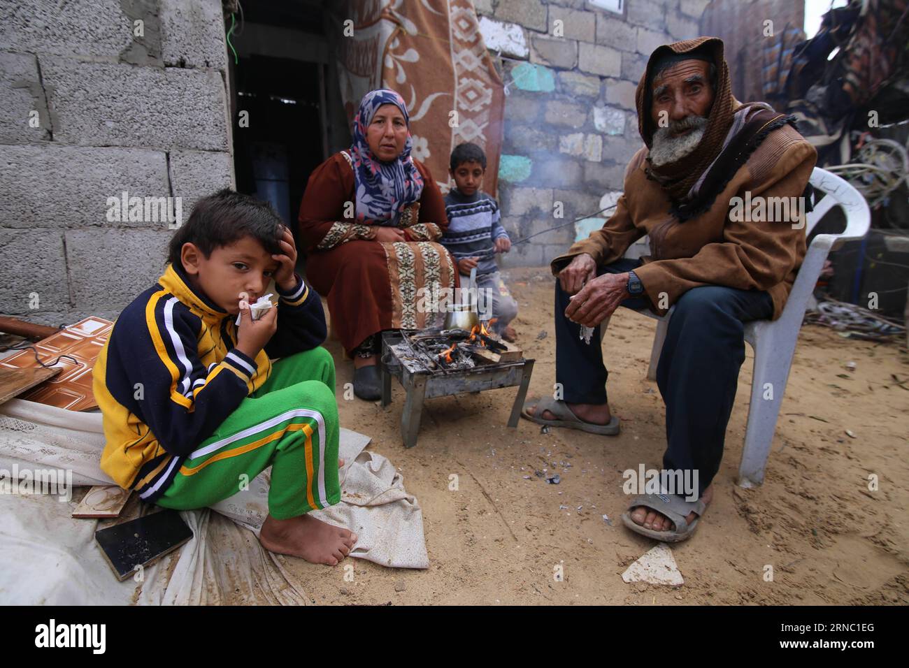(160317) -- GAZA, March 17, 2016 -- Palestinian Jihan Moussa Abu Mohsen, 48, sits with her family members near the fire inside their house in the southern Gaza Strip city of Khan Yunis, on March 17, 2016. Jihan, who works from the morning hours till late the day, sells a cart of bricks to stone manufacturers for 4 US dollars per day. Her work is the main source of income for her family which consists of her husband and four children. Jihan and her son Ahmad get up early every morning to collect bricks and stones from anywhere they find them, whether in landfills, streets or roadsides. Khaled O Stock Photo