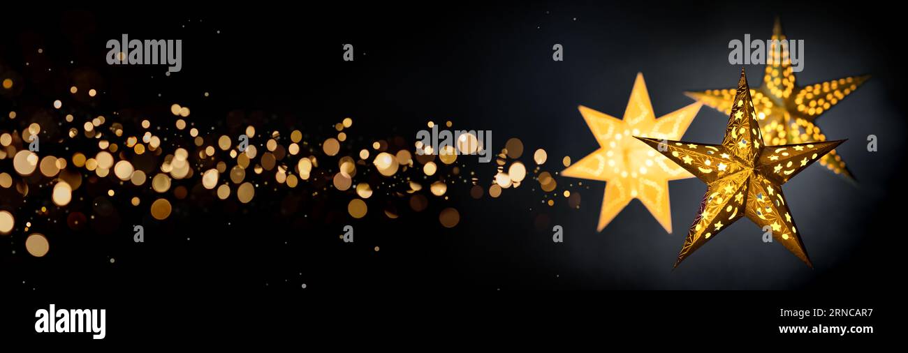 Ornamental gold star lanterns for Christmas on black background with golden bokeh stardust, extra wide format Stock Photo