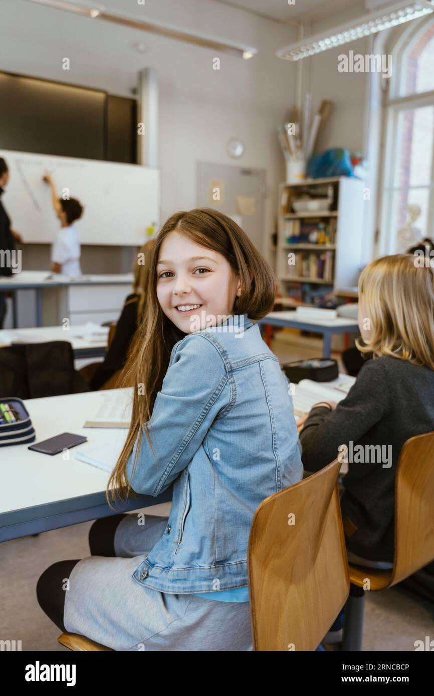 Side view portrait of smiling girl wearing denim jacket while sitting ...