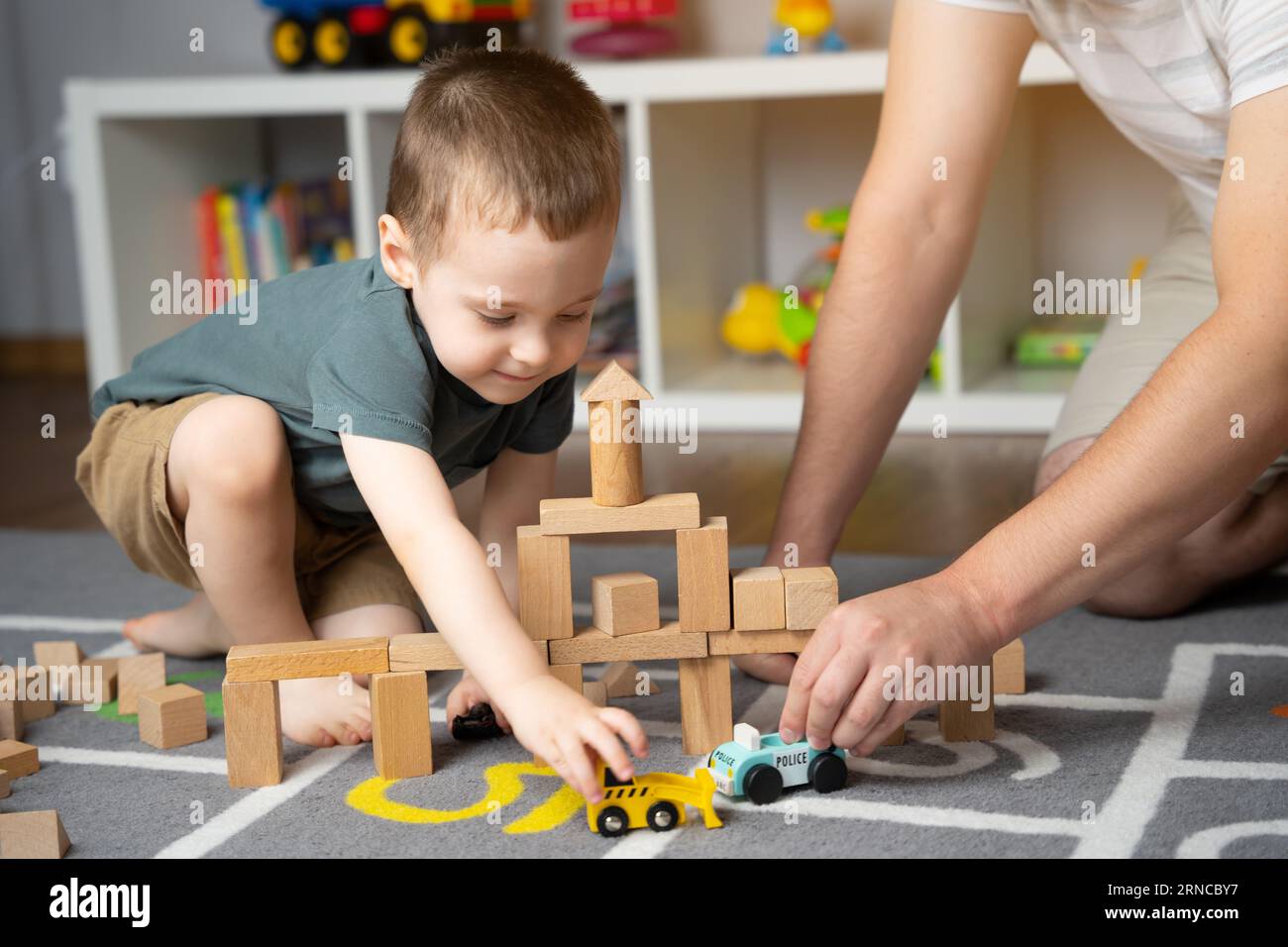 Little toddler boy 2,5 years playing wooden blocks and toy cars with dad. Spending time with children. Educational activities for kids. Children's roo Stock Photo