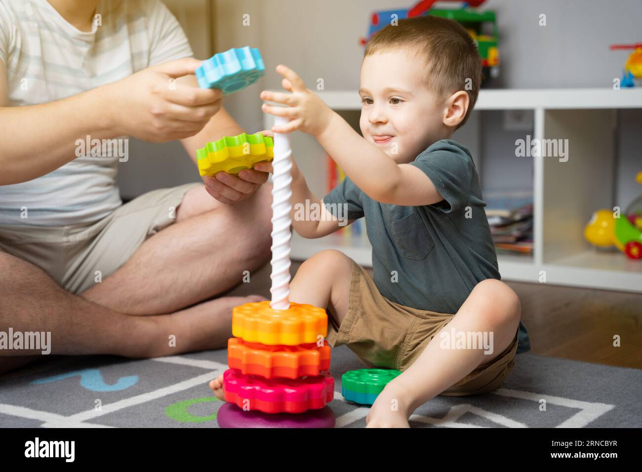 Happy smiling little toddler boy 2,5 years playing colorful pyramid with dad. Spending time with children. Educational toys for kids. Children's room. Stock Photo