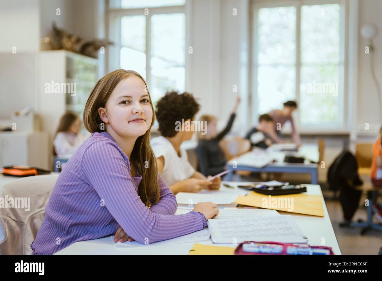 Portrait of smiling schoolgirl sitting at desk in classroom Stock Photo ...