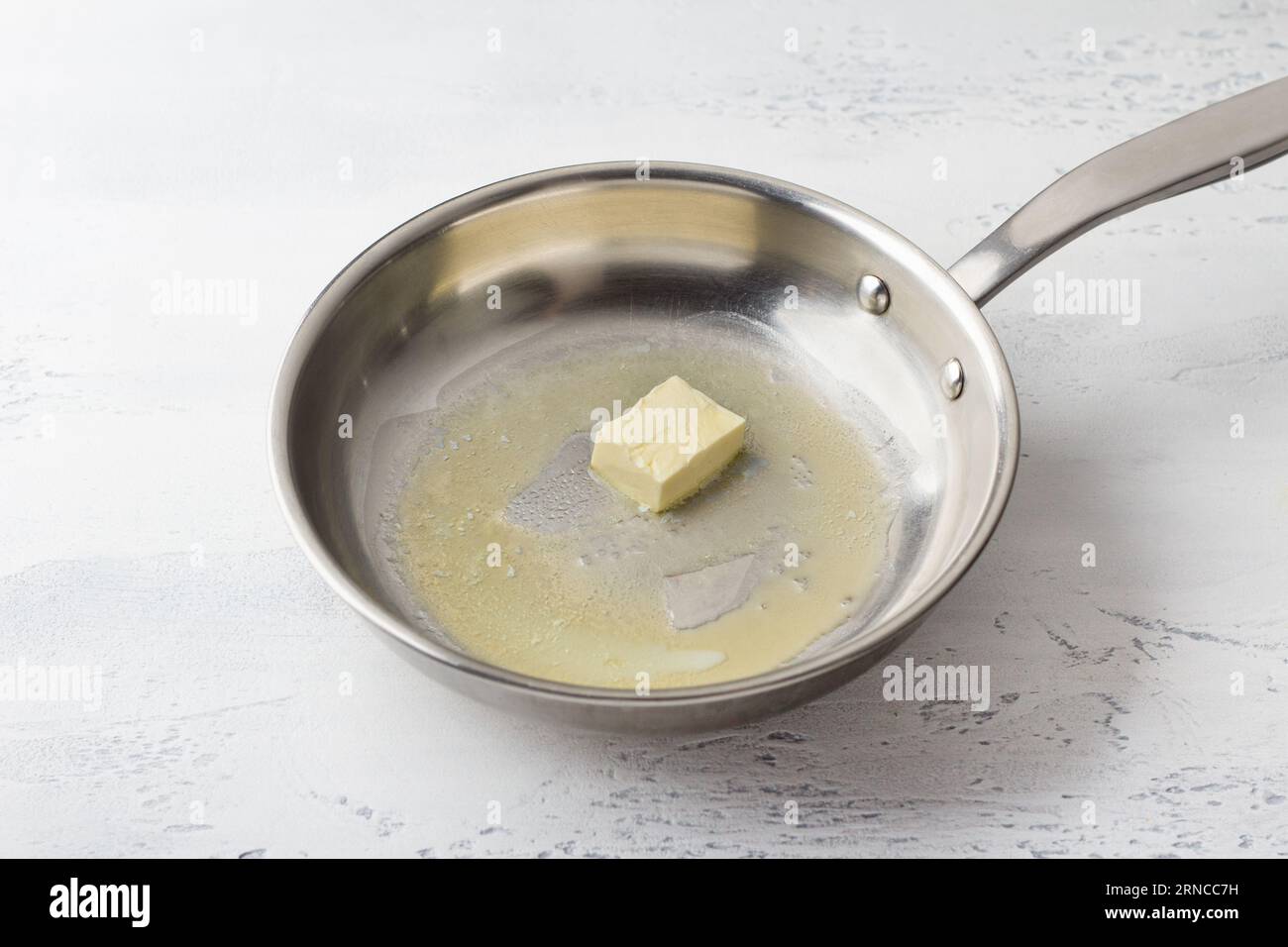 A piece of butter is melted in a frying pan on a light gray background. Making cheese pasta sauce, step by step, do it yourself, step 1 Stock Photo