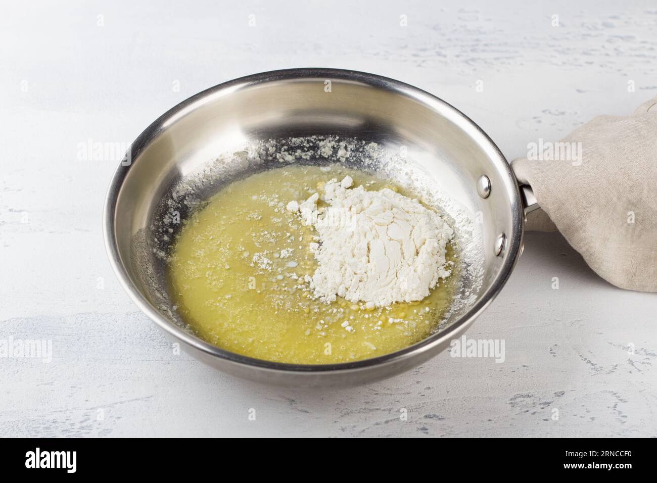 Flour is added to melted butter in a frying pan on a light gray background. Making cheese pasta sauce, step by step, do it yourself, step 2. Stock Photo