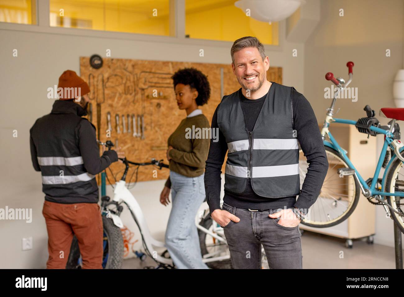 Portrait of happy male worker with hands in pockets during cycle repairing workshop at recycling center Stock Photo