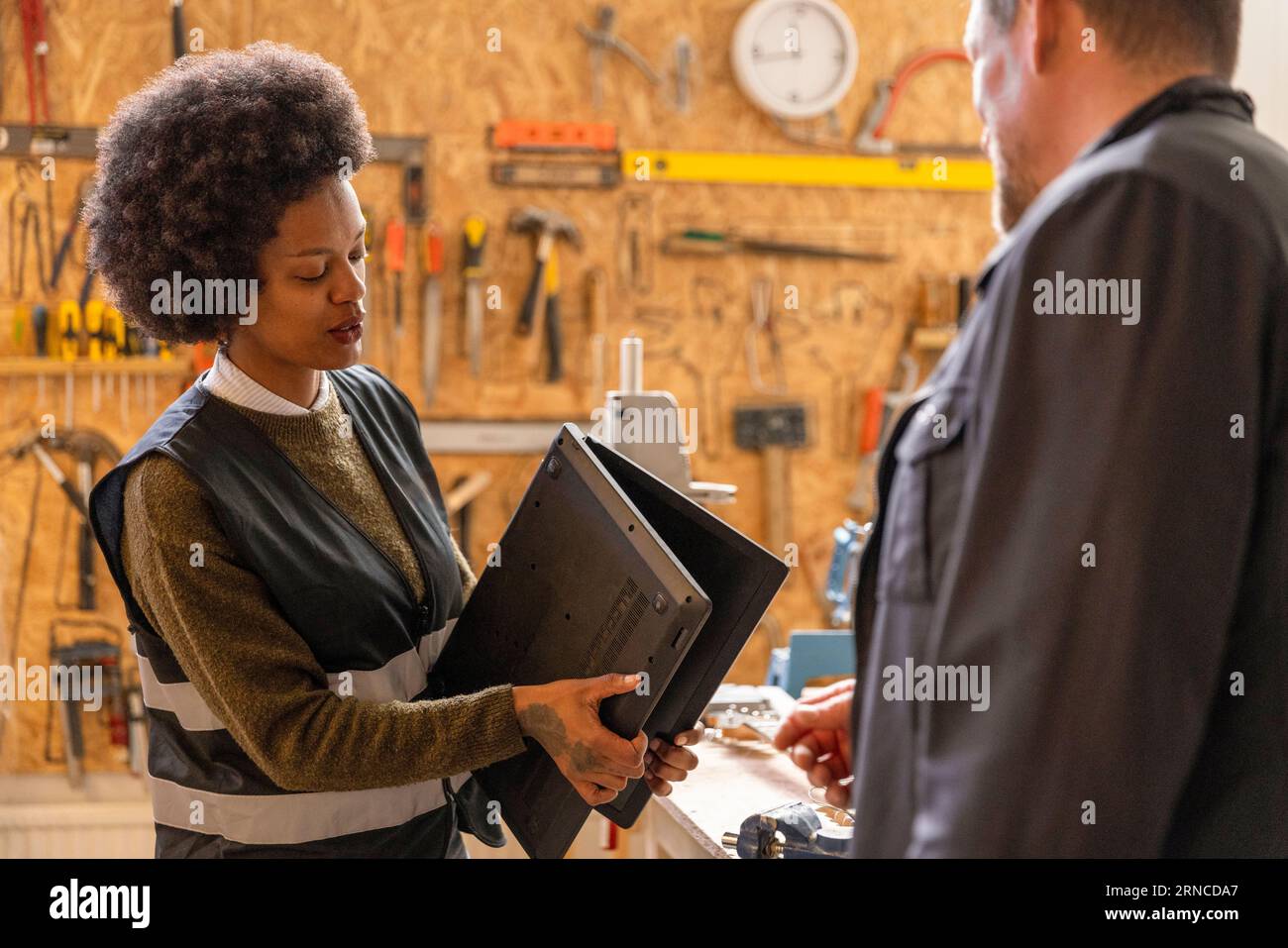 Female technician examining laptop while talking to customer at recycling center Stock Photo