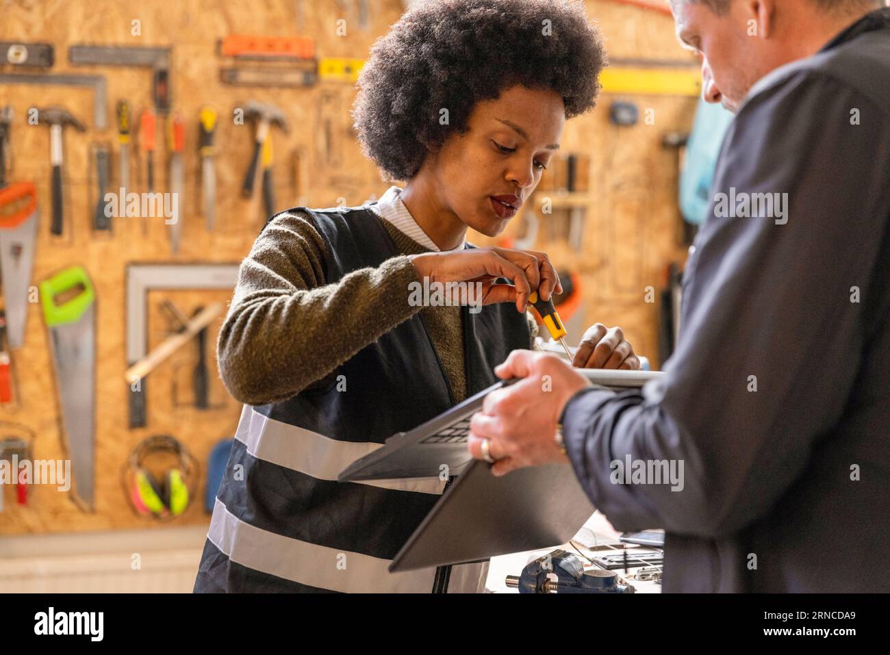 Focused female technician repairing laptop held by man at recycling center Stock Photo