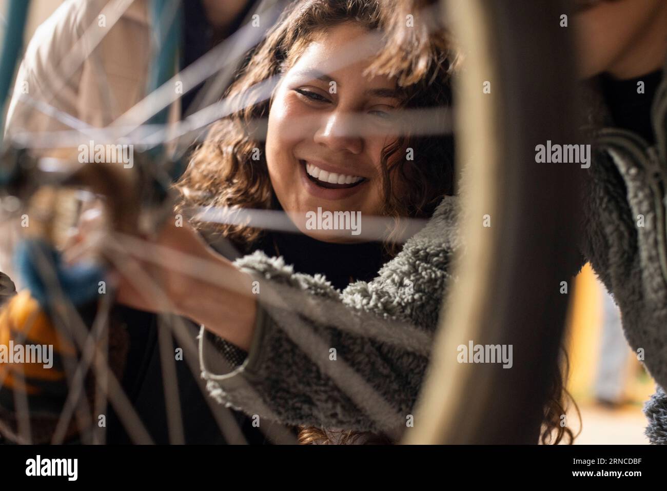 Happy female technician seen through bicycle wheel spokes at recycling center Stock Photo