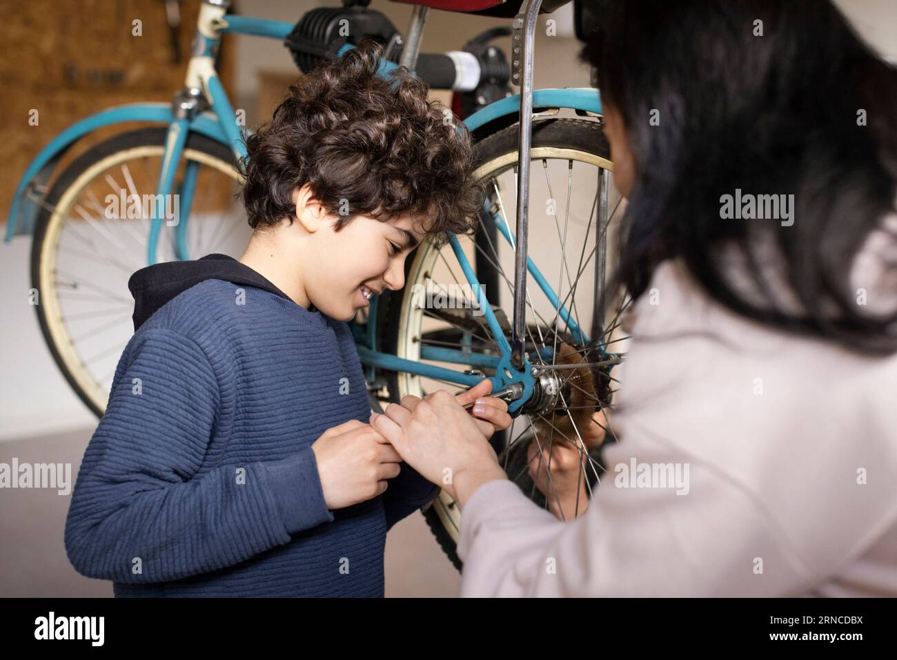 Smiling boy tightening screw of bicycle wheel with mother at recycling center Stock Photo