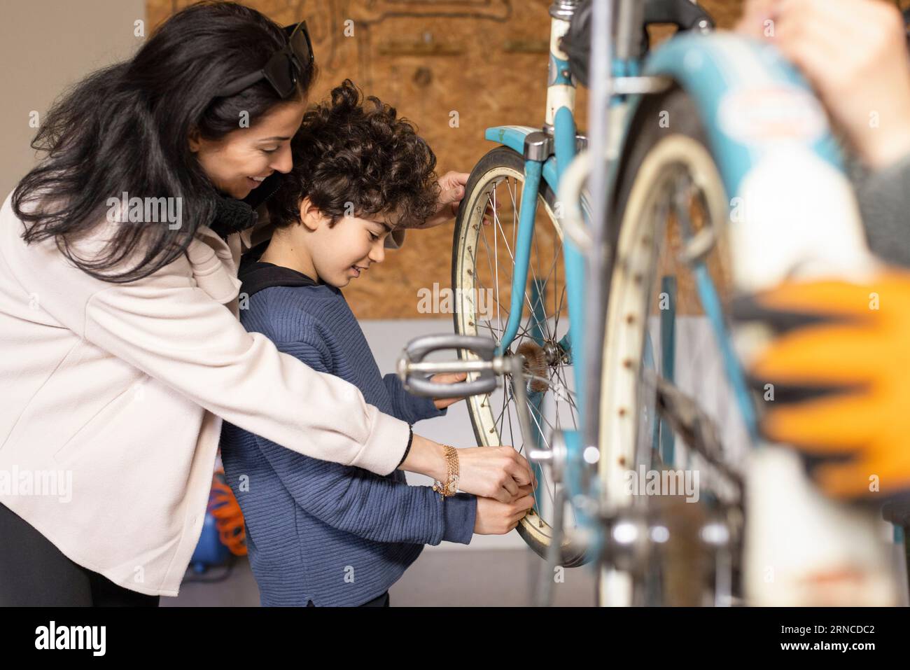 Side view of happy woman assisting son learning to repair bicycle at recycling center Stock Photo