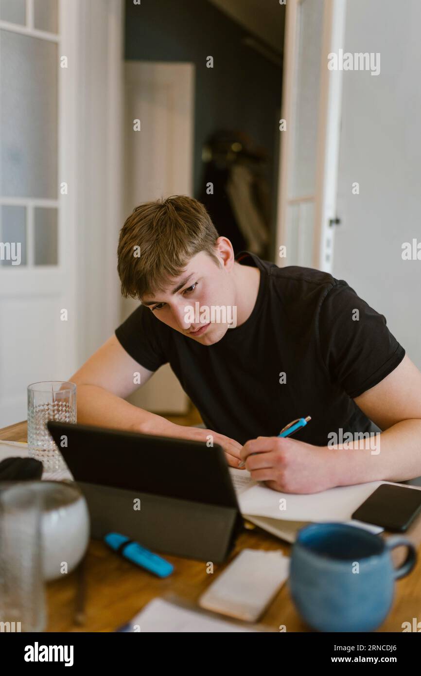 Young man writing while studying from digital tablet at home Stock Photo