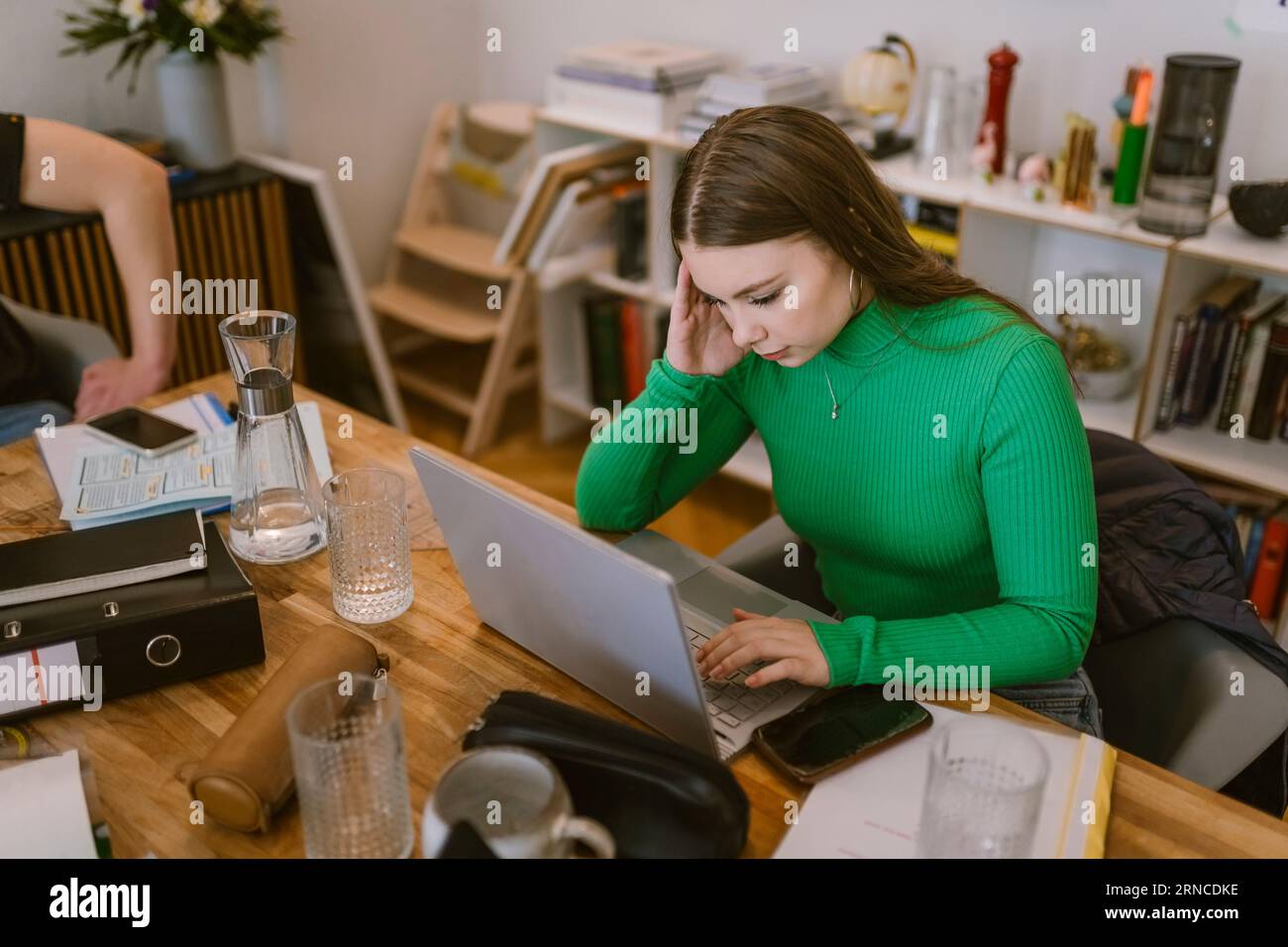 Young woman using laptop while doing school assignment at home Stock Photo