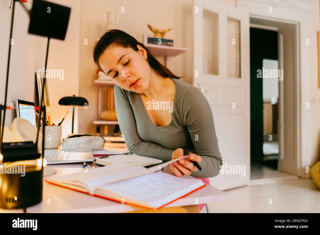 Young woman reading book while doing homework at table Stock Photo