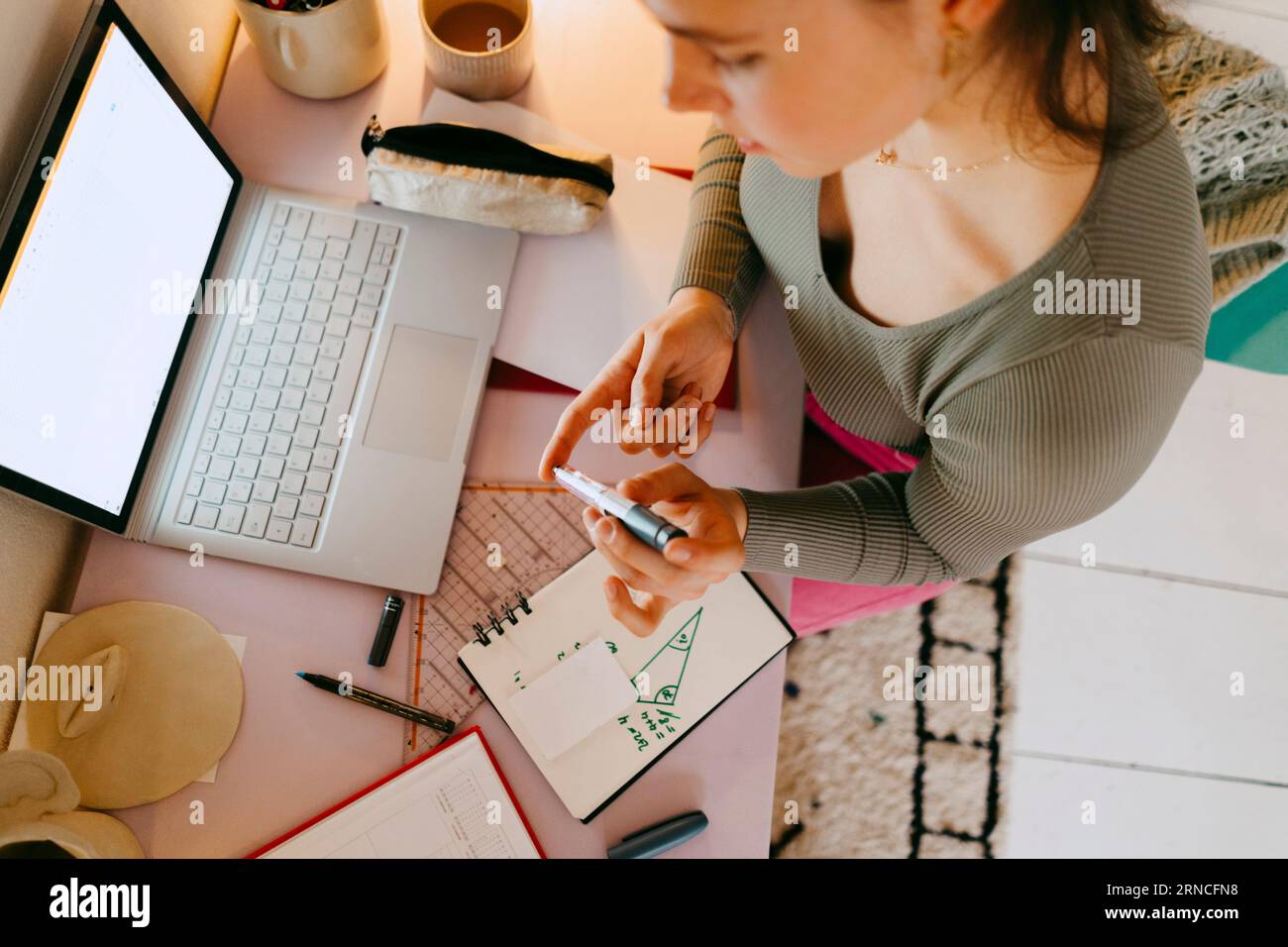 High angle view of young woman using glucometer while doing homework at table Stock Photo