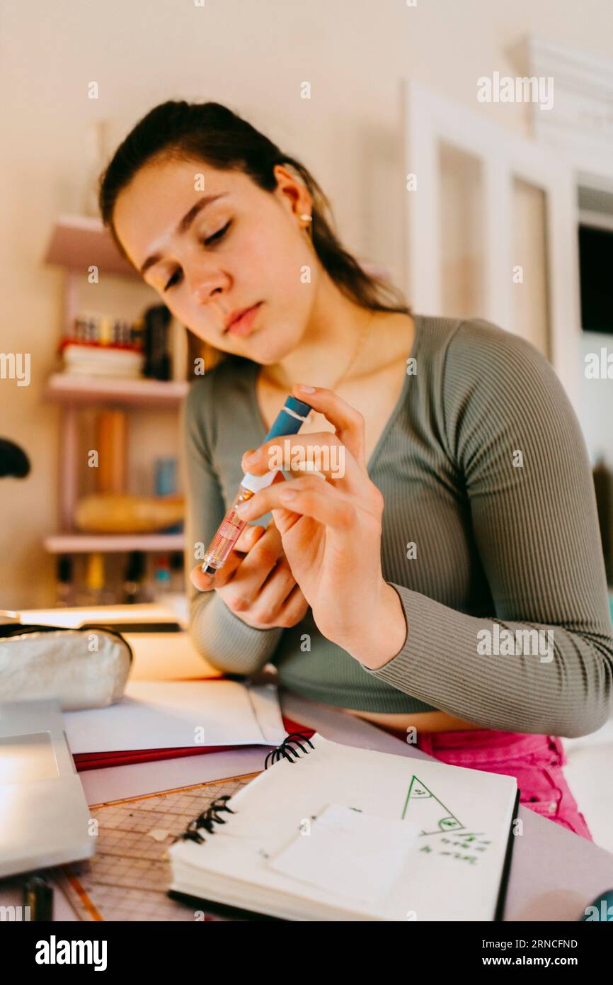 Young woman using glucometer while doing homework at home Stock Photo