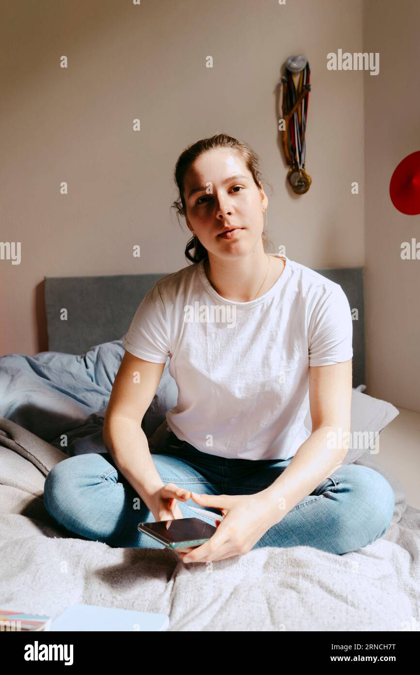 Portrait of young woman sitting on bed at home Stock Photo