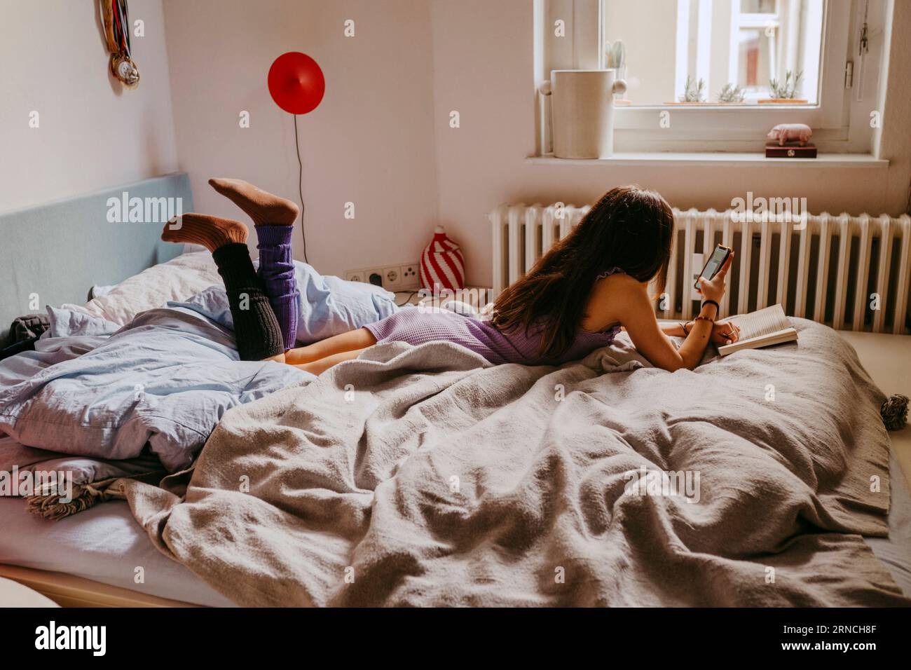 Young woman using mobile phone while lying on bed at home Stock Photo