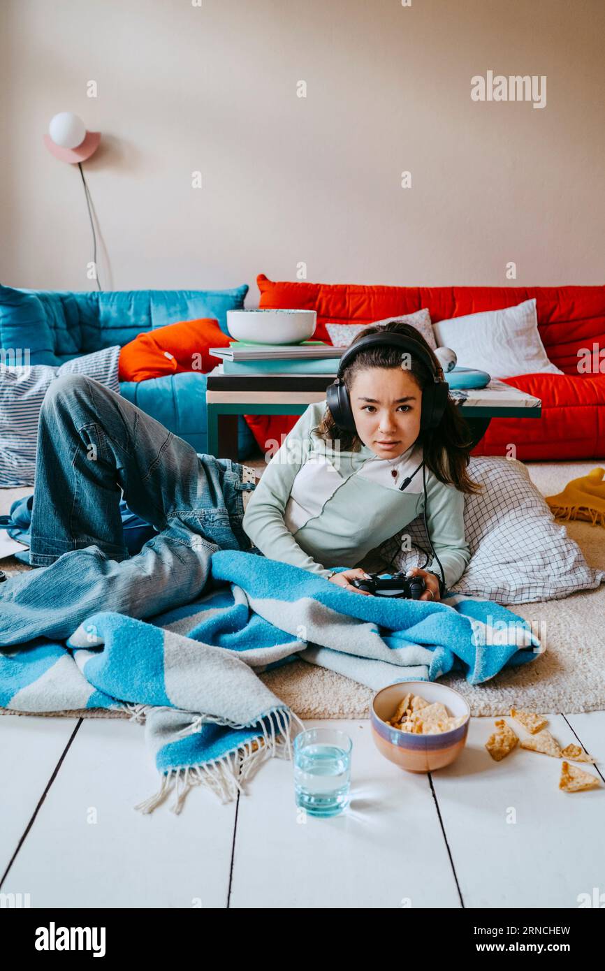 Young woman playing video game while lying in living room at home Stock Photo