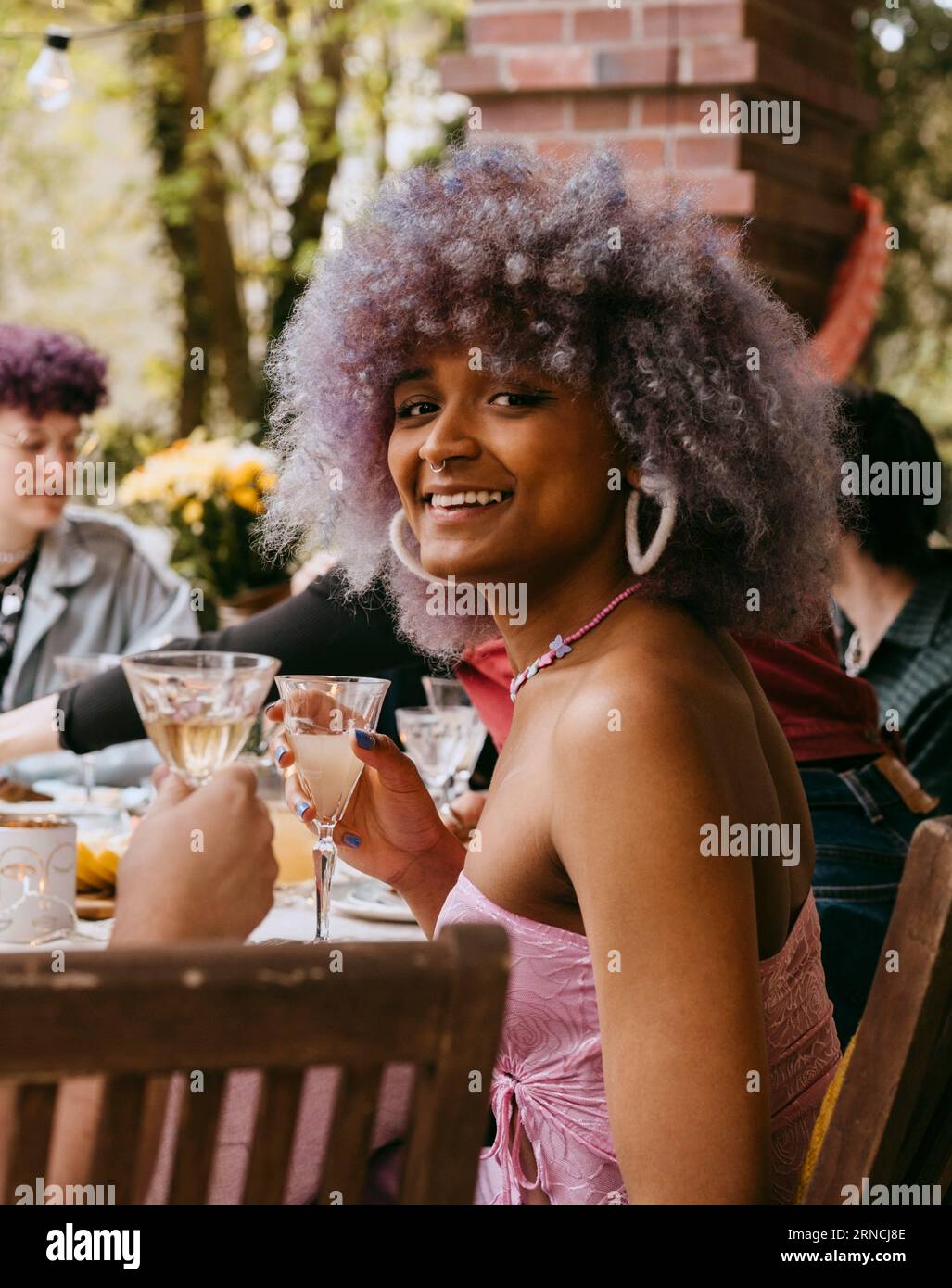 Side view portrait of smiling transwoman with curly hair sitting with friends during party in back yard Stock Photo