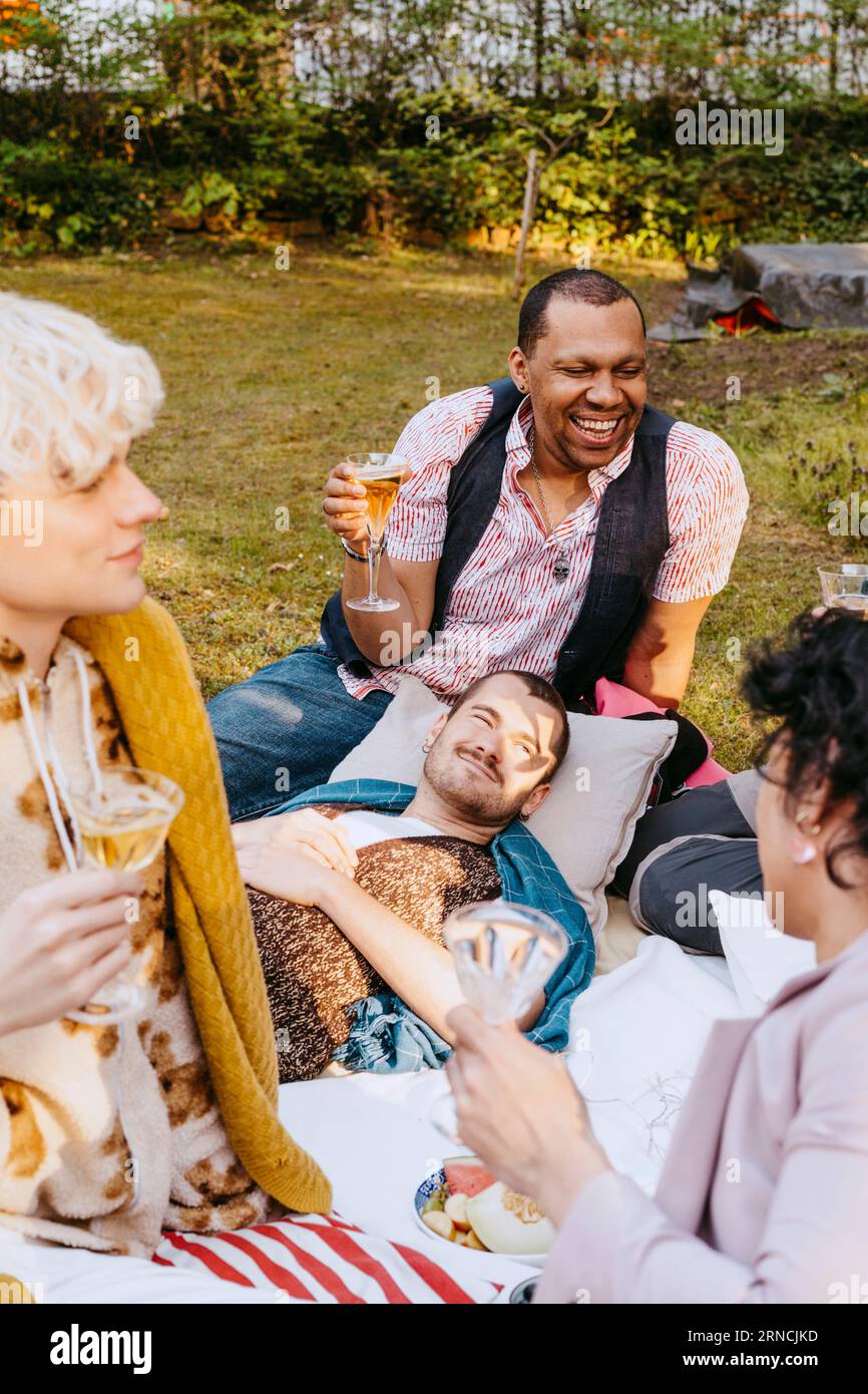 Happy gay man enjoying drinks with LGBTQ friends in back yard Stock Photo