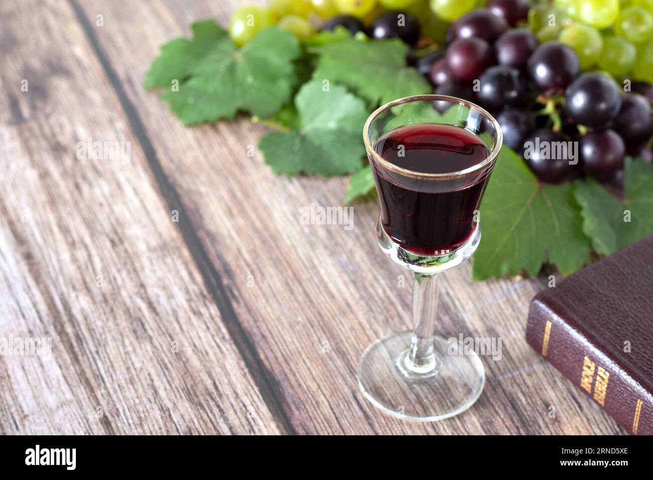 Glass of red wine, grapes, and holy bible book on wooden table. Copy space. Close-up. Stock Photo