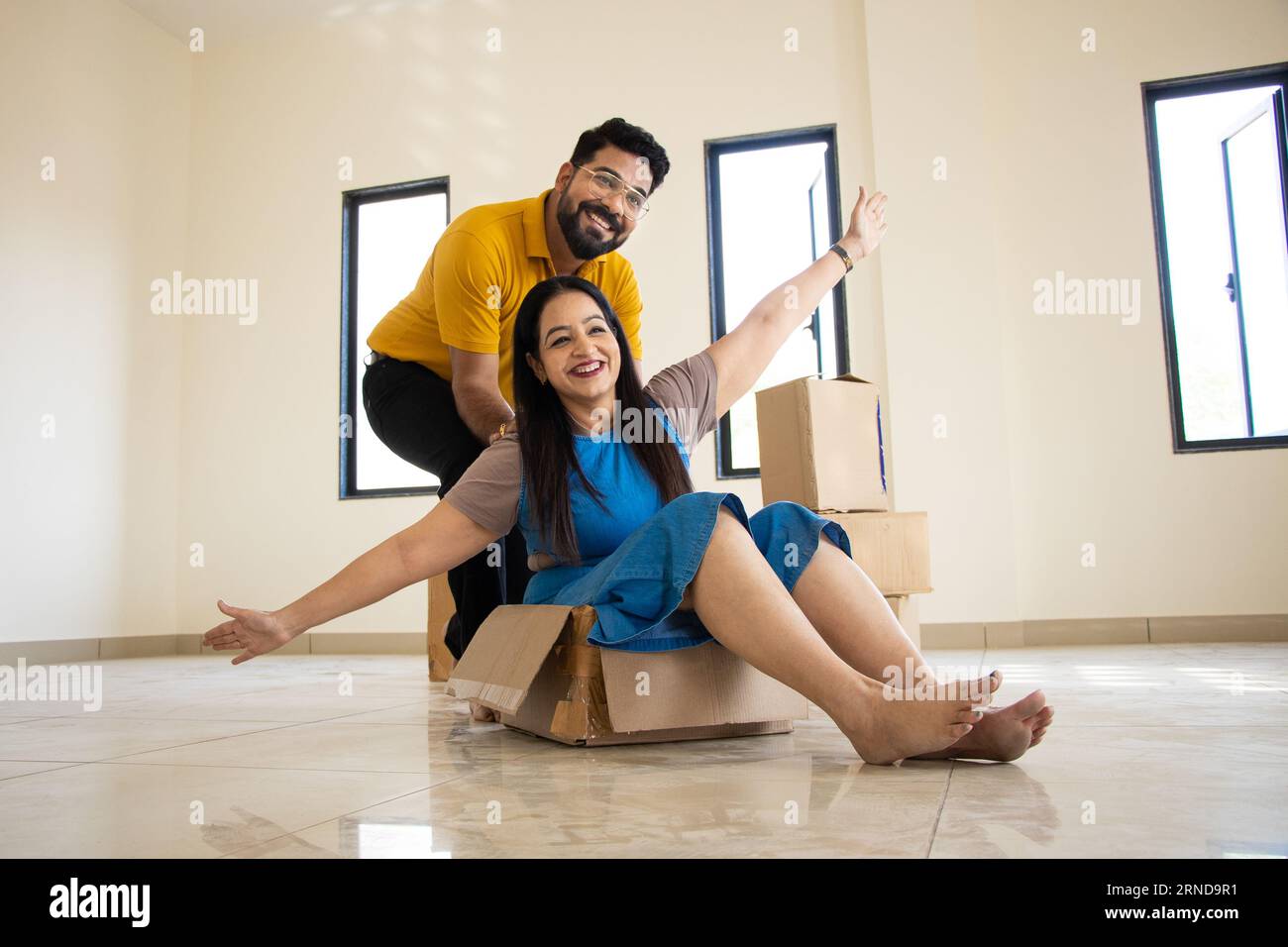 Happy young indian couple having fun in new home. Playing with boxes, Real estate, residential mortgage, moving into dream house concept. Stock Photo