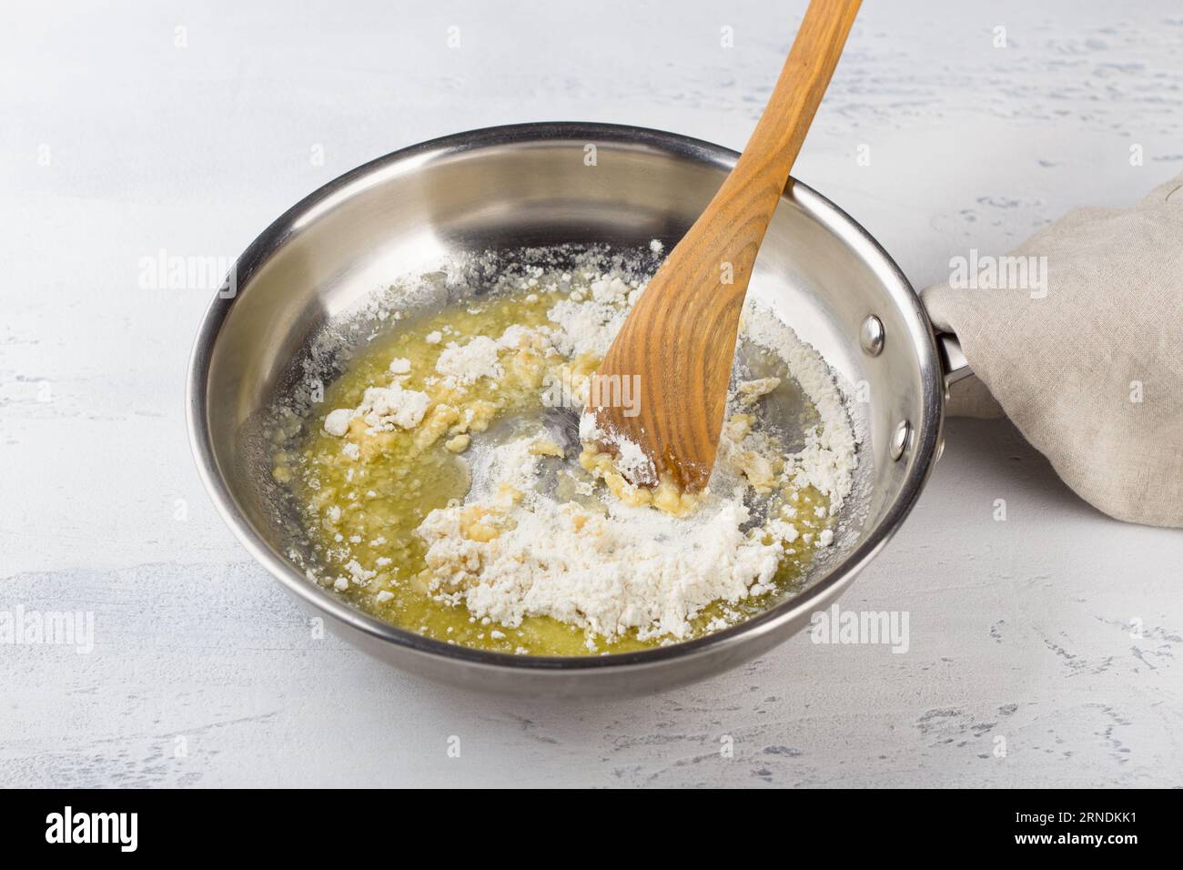 Mixing flour with melted butter in a frying pan on a light gray table. Making cheese pasta sauce, step by step, do it yourself, step 3 Stock Photo