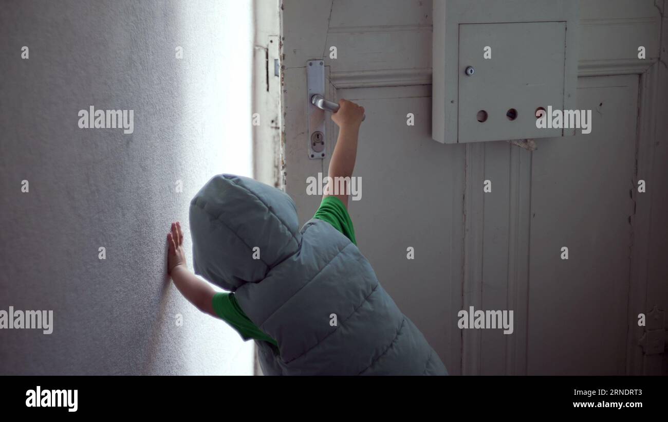 Child opening front door of home and stepping out in street. One little