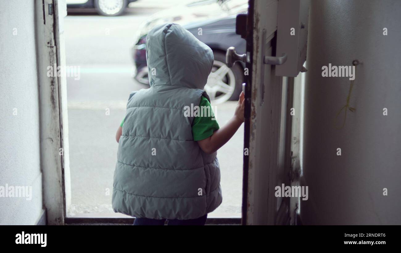 Child opening front door of home and stepping out in street. One little