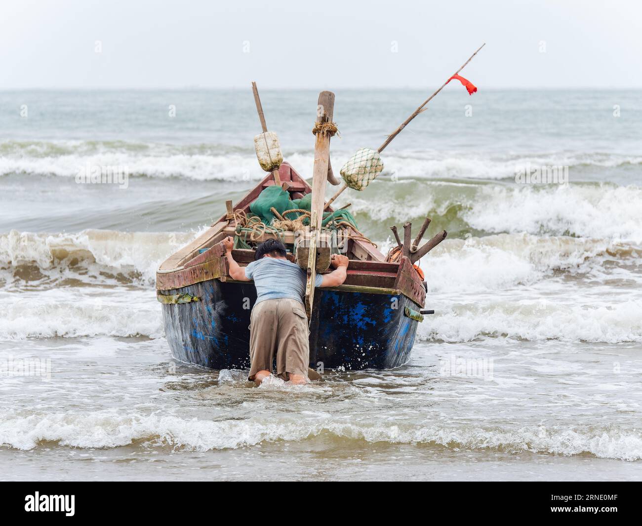Fisherman launching his boat against wind and high waves in Sam Son Beach, Thanh Hoa, Vietnam Stock Photo