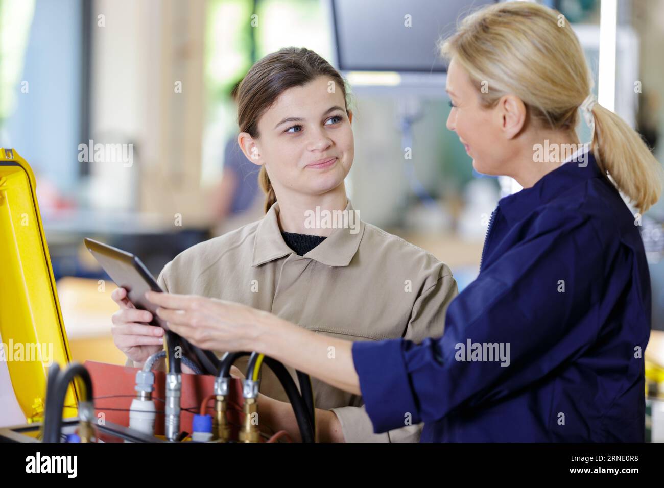 female apprentice and instructor using digital tablet in factory Stock Photo