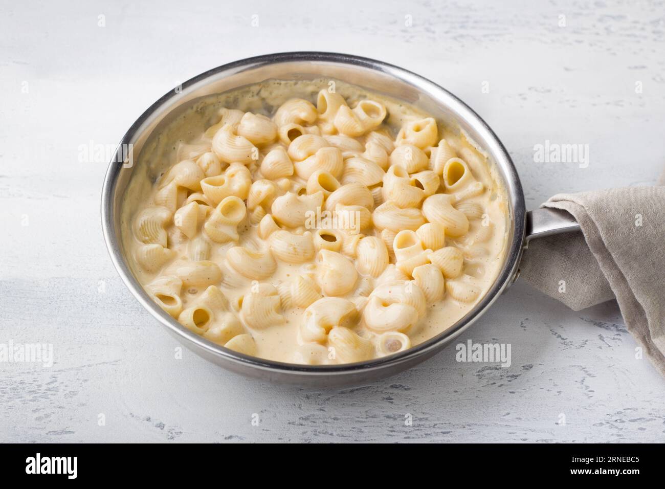 Cooking mac and cheese, American pasta. Adding cooked pasta to cheese sauce in a frying pan on a light gray background. Cooking stage Stock Photo