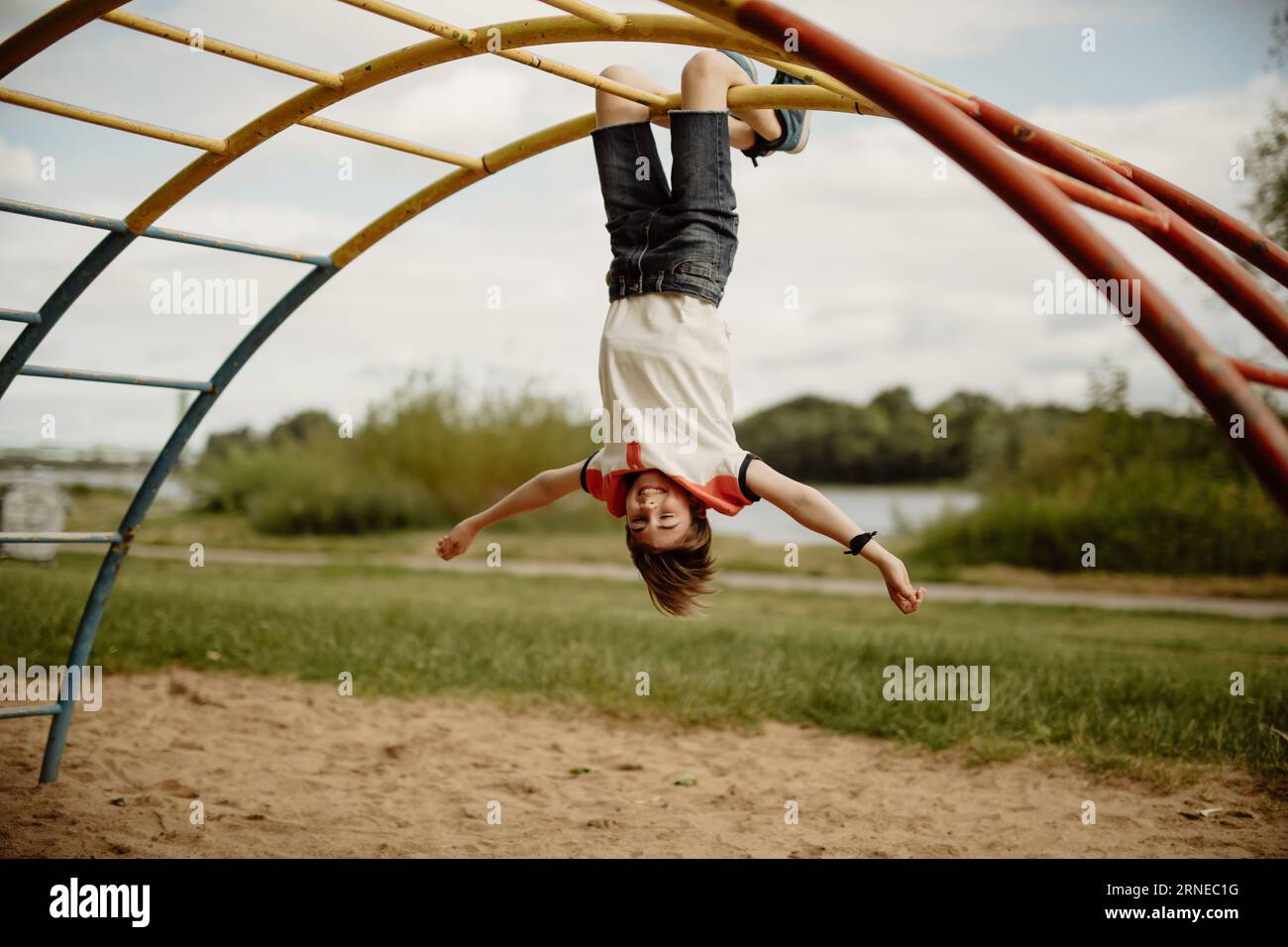 happy teen boy enjoy childhood by hanging upside down from pole of a climbing frame on playground Stock Photo