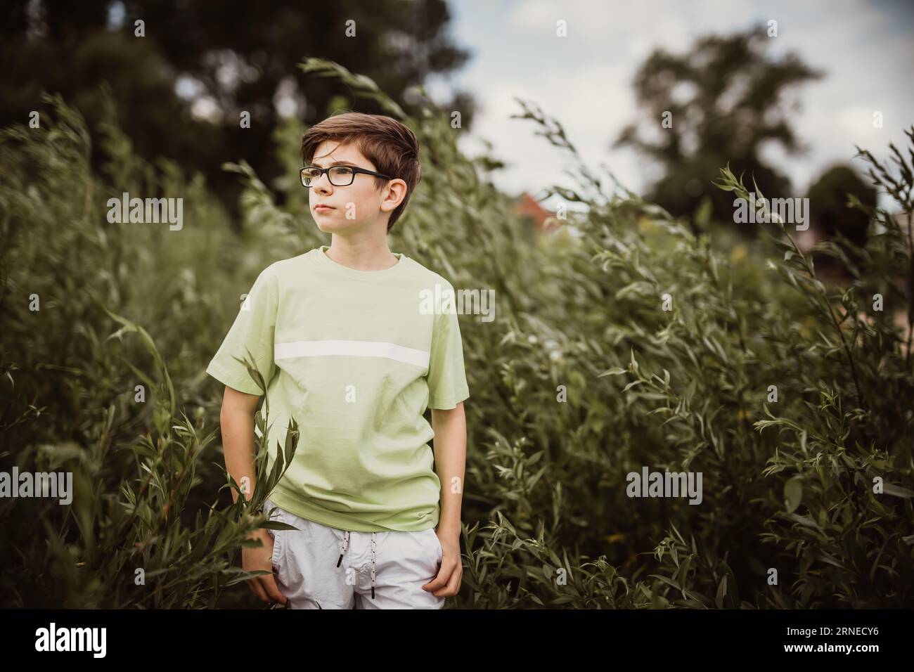 teen boy walk in green field between trees while enjoy childhood but being in thoughts about depression and sadness Stock Photo
