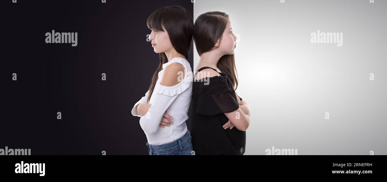 good and bad sisters wear black and white shirts and stand back to back with crossed arms look forward to side and show contrast between family member Stock Photo