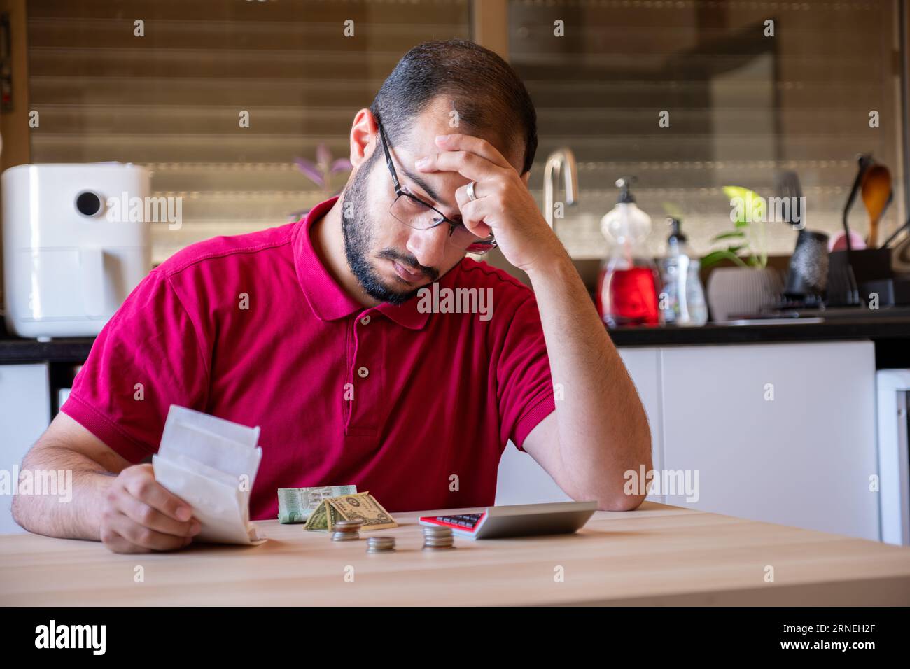 man sitting in the kitchen and calculating the costs of living feeling frustrated Stock Photo