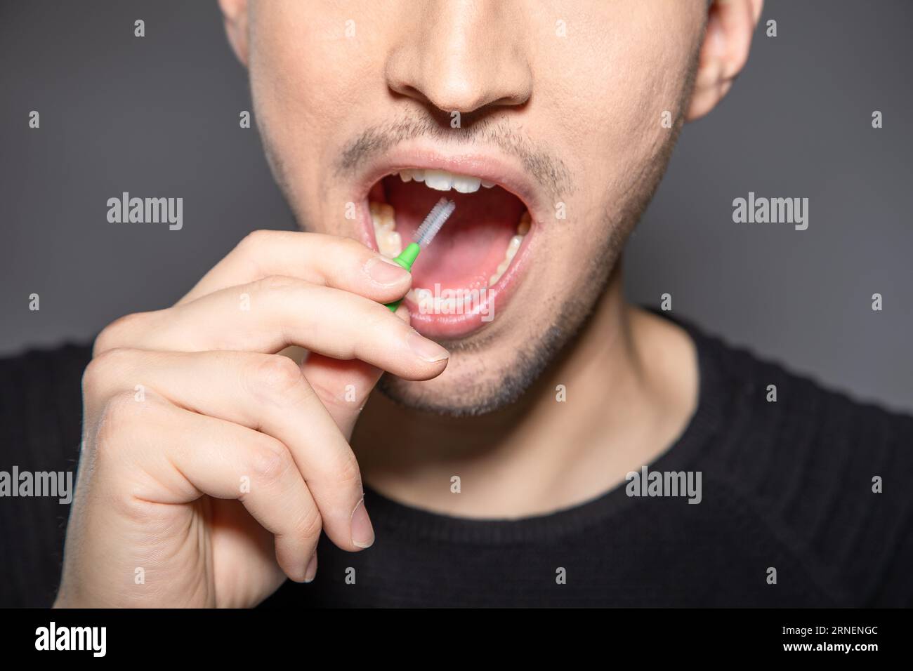 man with interdental tooth brush hold handle into open mouth ready to