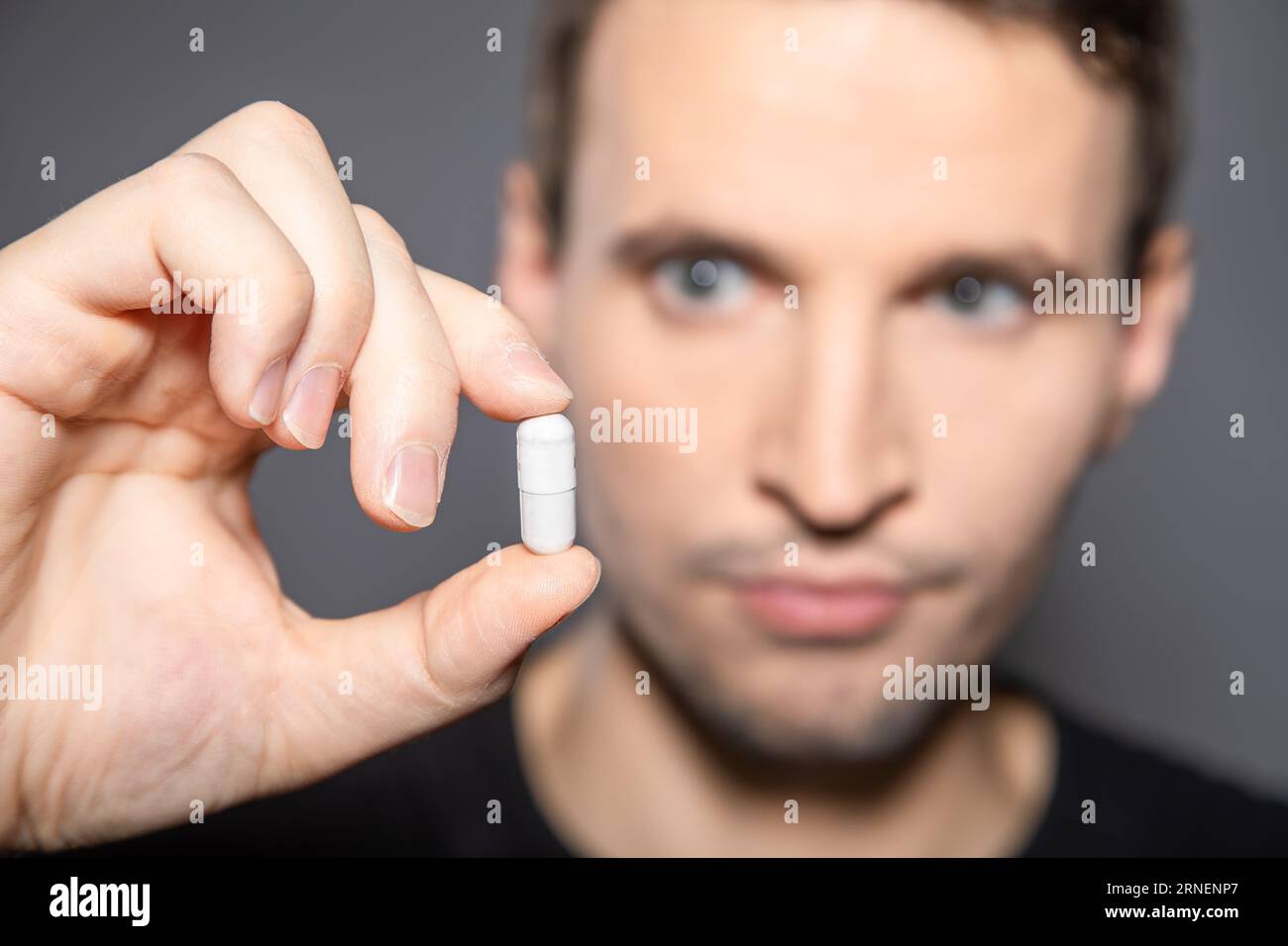 man look at big white capsule pill in his hand afraid to swallow this