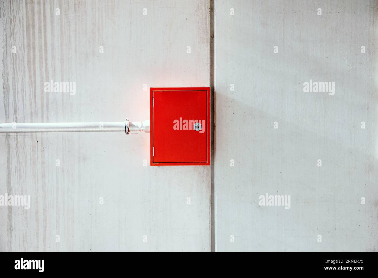 closed red metal box including fire extinguisher and fire hose hang on rough and grungy concrete wall with pipe from side supplying extinguishing wate Stock Photo