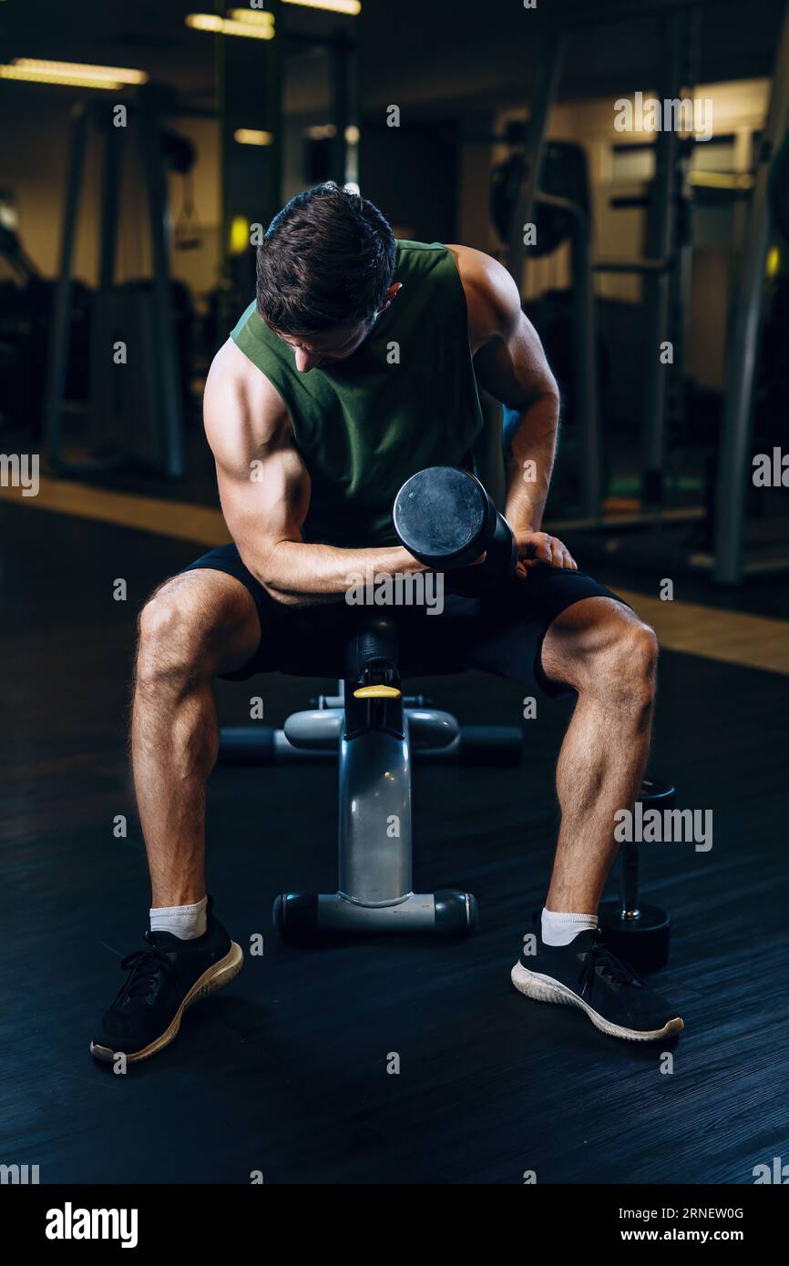 lift dumb bell at gym sitting on machine and look to arm while gaining muscles Stock Photo