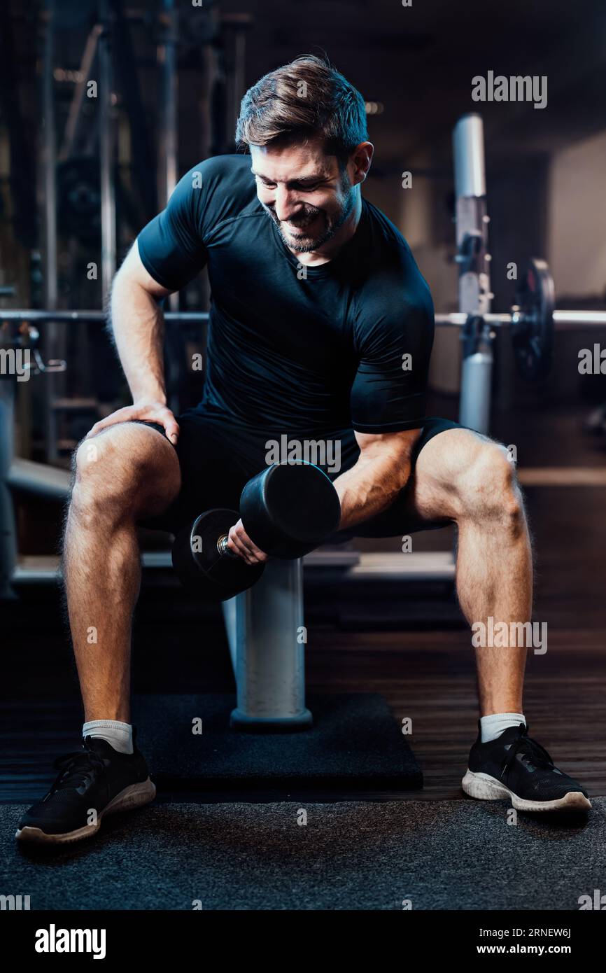 visible pain at face of this sportive man while lifting dumb bells and effort gaining muscles Stock Photo