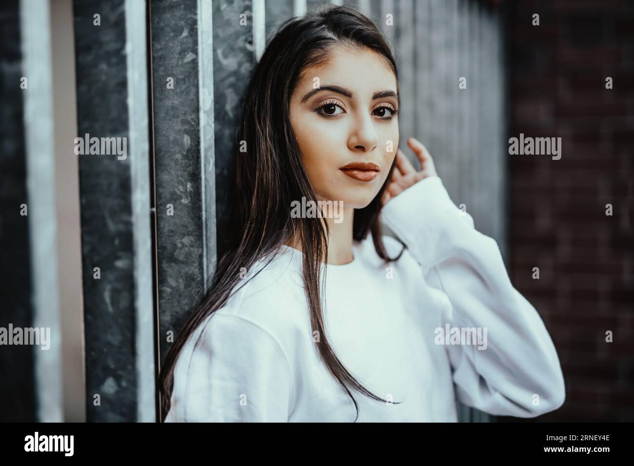 worried teenager girl with hand at head look at camera think about being a bullied victim and stand confident in front of fence Stock Photo