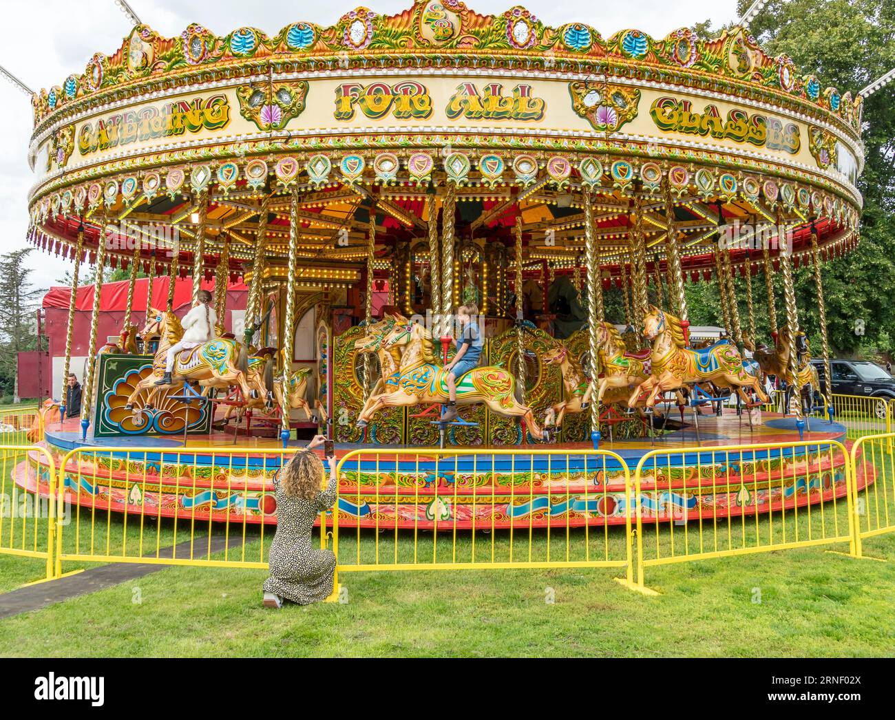 Woman photographing children on fairground Galloper ride, The Lawn, Lincoln City, Lincolnshire, England, UK Stock Photo