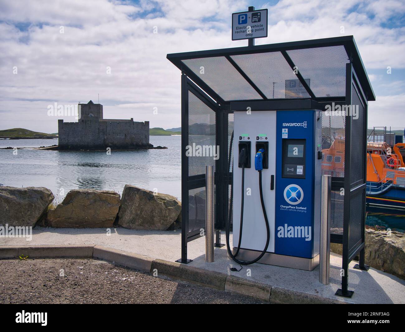 A SWARCO ChargePlace Scotland EV charging point at the harbour of Castlebay on the island of Barra in the Outer Hebrides, Scotland, UK. Kisimul Castle Stock Photo