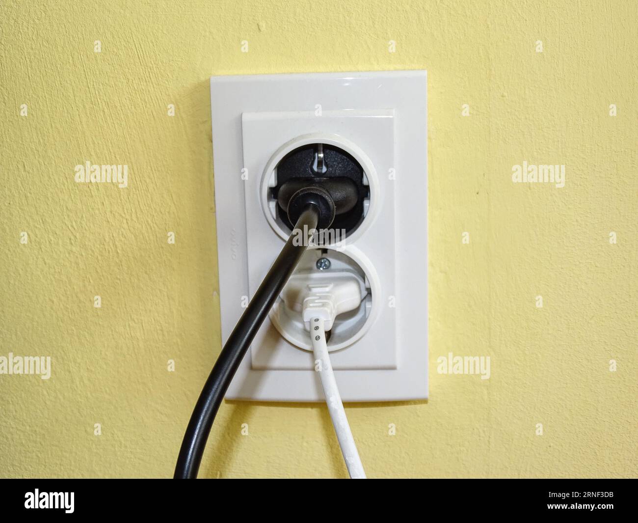 A black plug and a white plug in the socket Stock Photo