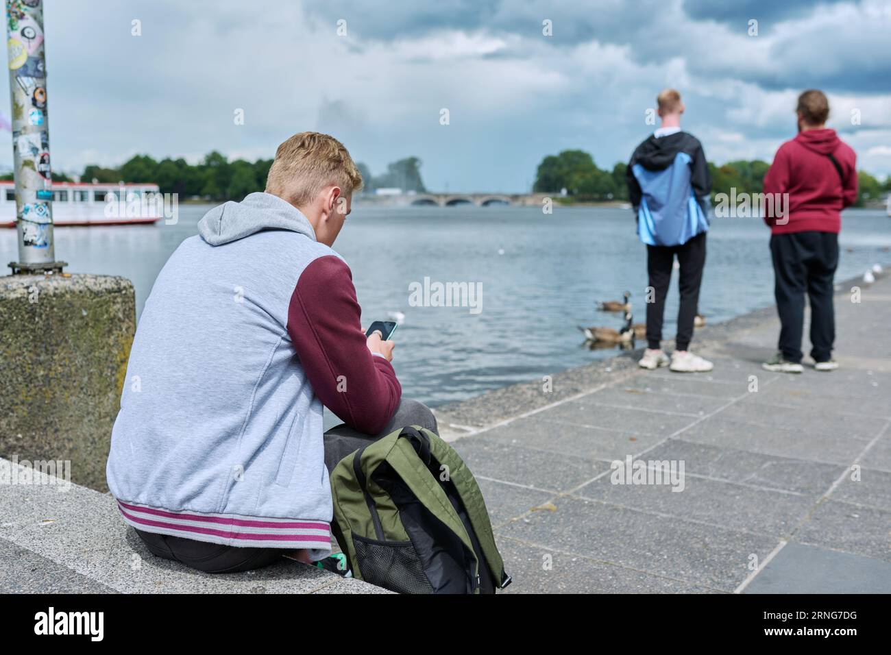 Young guy texting on smartphone, back view, sitting on city embankment ...