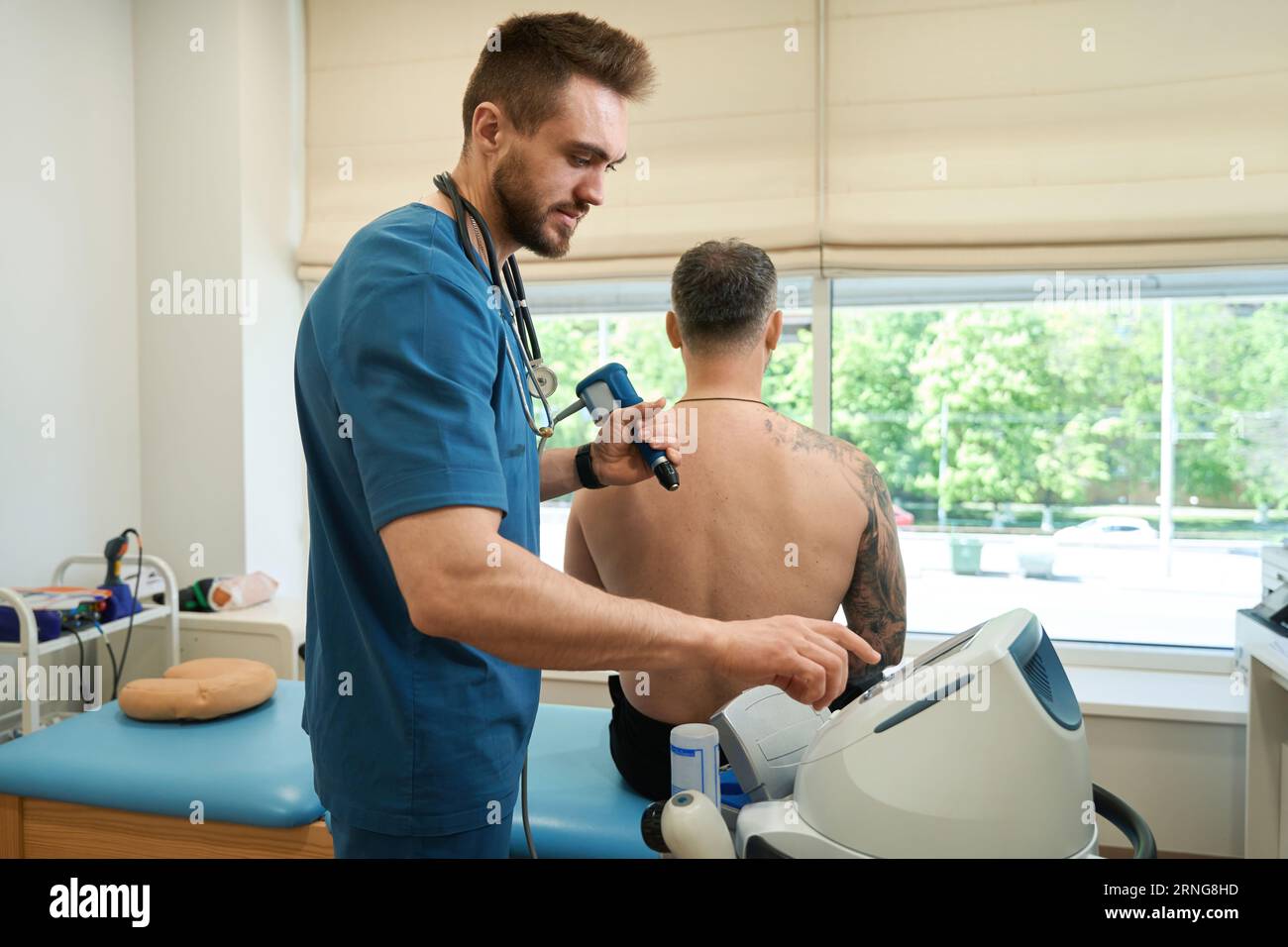 Experienced physical therapist preparing adult man for ESWT session Stock Photo
